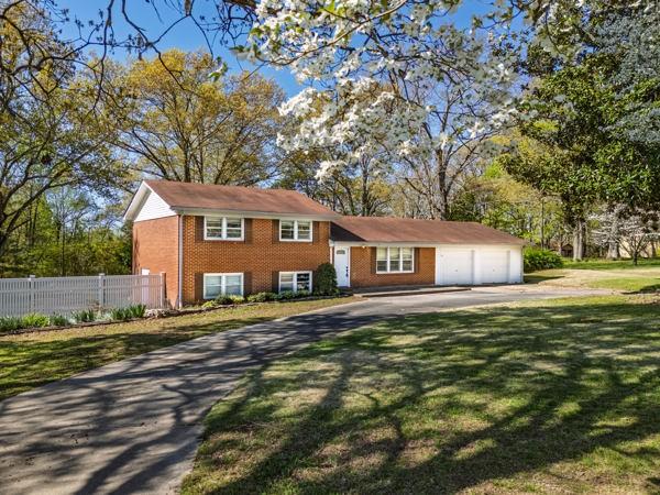 tri-level home featuring concrete driveway, a front yard, brick siding, a garage, and fence