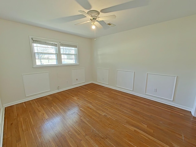 spare room with baseboards, a ceiling fan, visible vents, and hardwood / wood-style flooring