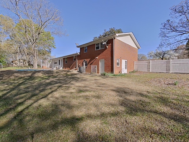 rear view of house with a yard, brick siding, fence, and central AC unit