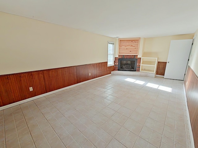 unfurnished living room with wood walls, wainscoting, and a brick fireplace