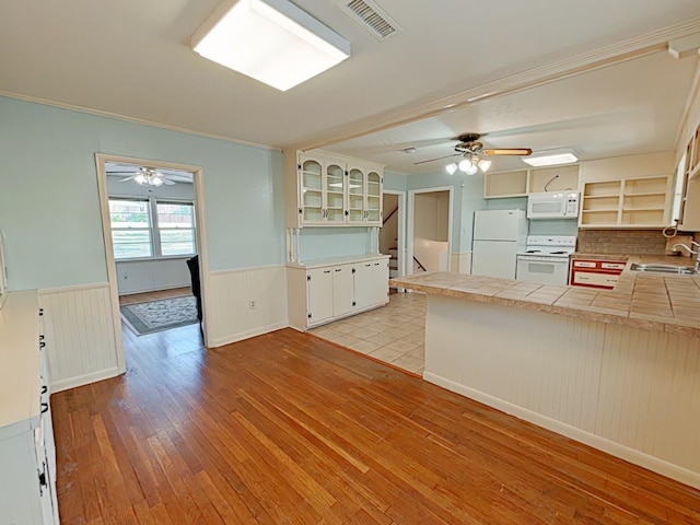kitchen featuring visible vents, a sink, white appliances, light wood finished floors, and a wainscoted wall