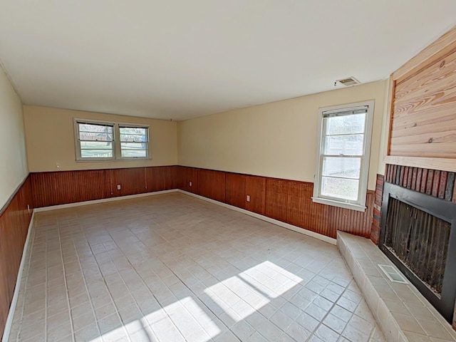 empty room featuring wood walls, a fireplace, and wainscoting