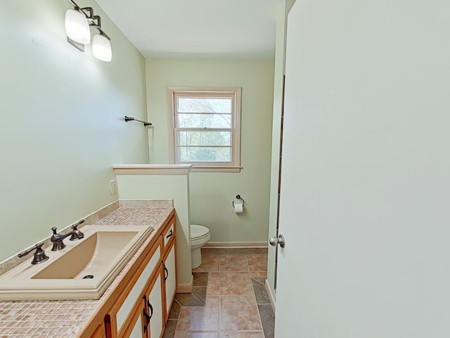 bathroom featuring toilet, a shower, vanity, and baseboards