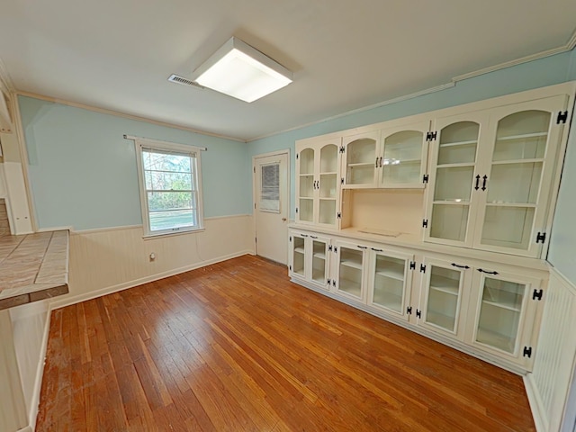 interior space featuring crown molding, visible vents, a wainscoted wall, and wood-type flooring