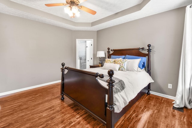 bedroom with a raised ceiling, wood finished floors, and a textured ceiling