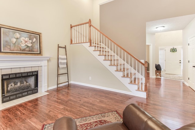 living room featuring a fireplace, stairway, baseboards, and wood finished floors