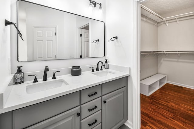 bathroom featuring a walk in closet, double vanity, a sink, and wood finished floors