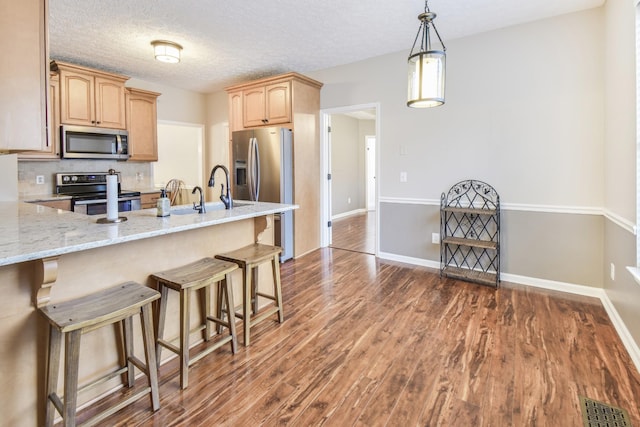kitchen featuring dark wood finished floors, appliances with stainless steel finishes, light stone counters, a breakfast bar area, and light brown cabinets