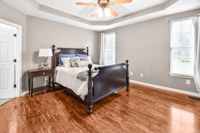 bedroom featuring a tray ceiling, a textured ceiling, and wood finished floors