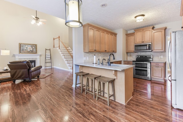 kitchen with a kitchen breakfast bar, a peninsula, appliances with stainless steel finishes, a sink, and dark wood-style floors