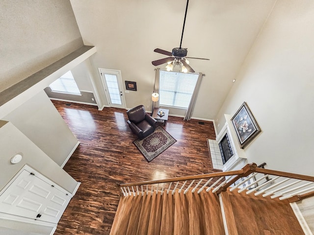 living room with a towering ceiling, baseboards, a ceiling fan, stairs, and wood finished floors
