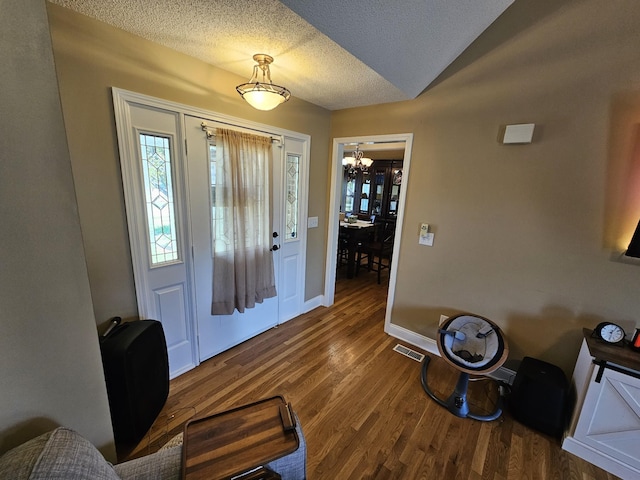 foyer featuring a textured ceiling, visible vents, baseboards, wood finished floors, and a notable chandelier