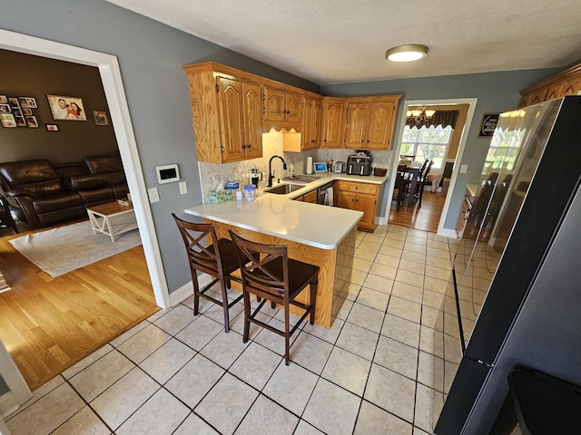 kitchen with freestanding refrigerator, light countertops, a sink, a peninsula, and light tile patterned flooring