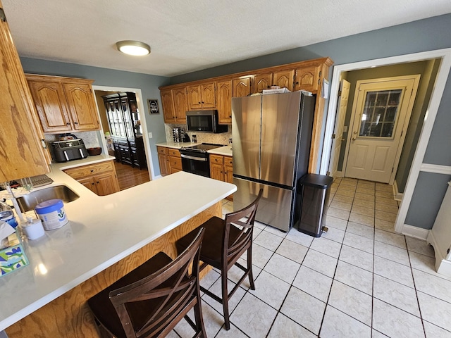 kitchen with tasteful backsplash, a peninsula, light countertops, freestanding refrigerator, and black range with electric cooktop