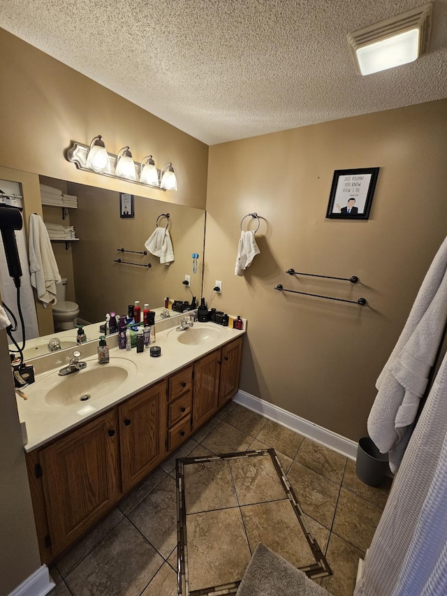 full bath with toilet, double vanity, a sink, and a textured ceiling