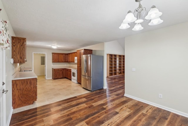 kitchen with a notable chandelier, a sink, light countertops, white appliances, and light wood-style floors