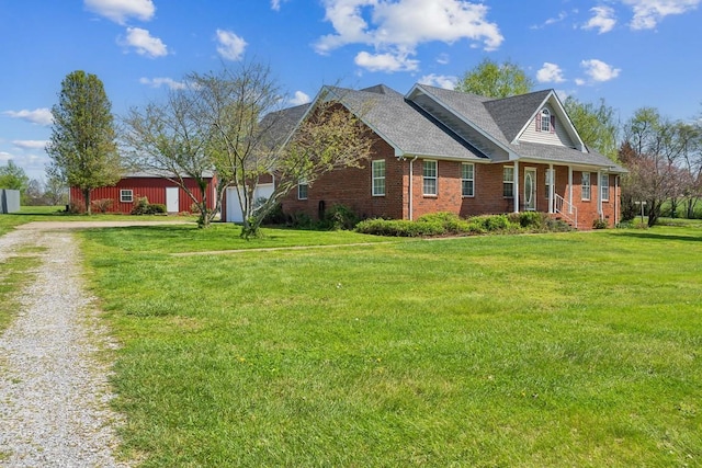 view of front of property featuring roof with shingles, brick siding, a front lawn, and dirt driveway