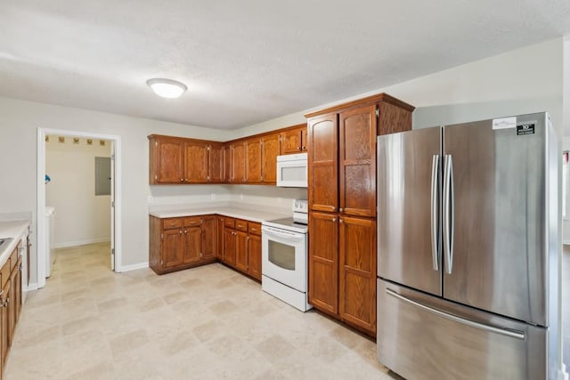 kitchen featuring brown cabinets, light countertops, white appliances, and baseboards