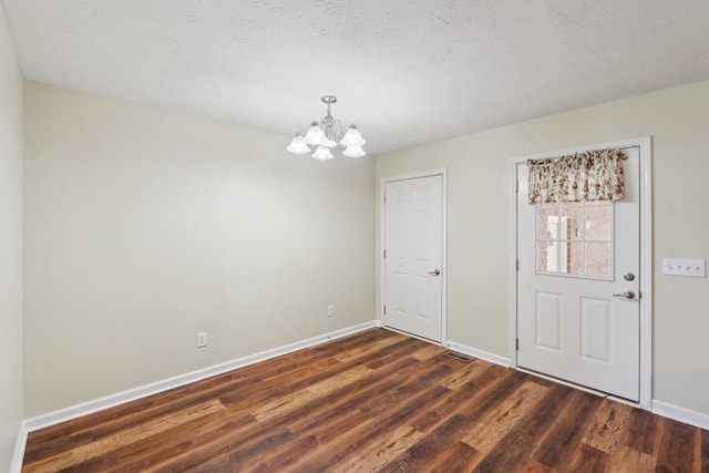 unfurnished room with visible vents, baseboards, a chandelier, and dark wood-style floors