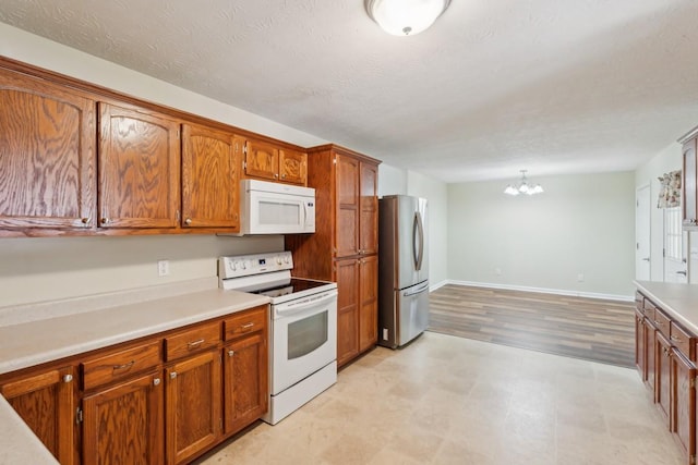 kitchen with brown cabinetry, light countertops, white appliances, and a chandelier