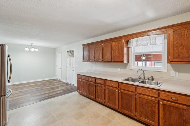 kitchen featuring a notable chandelier, a sink, light countertops, freestanding refrigerator, and brown cabinetry