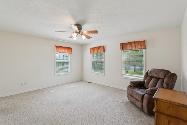 living area featuring light carpet, ceiling fan, baseboards, and a textured ceiling