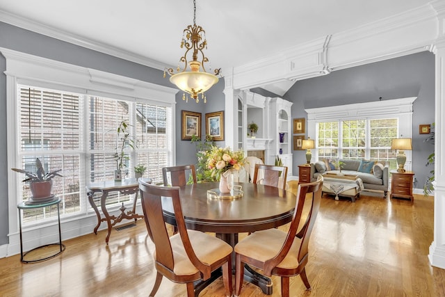 dining room with light wood-type flooring, a fireplace, crown molding, and baseboards