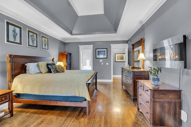 bedroom with baseboards, a tray ceiling, ornamental molding, and wood finished floors