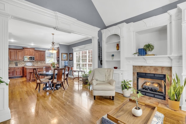 living room featuring light wood-style floors, a tiled fireplace, crown molding, and lofted ceiling