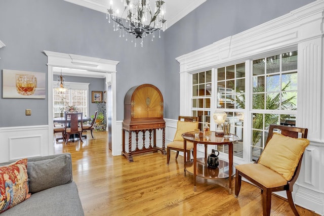 sitting room featuring an inviting chandelier, crown molding, a wainscoted wall, light wood-style floors, and a decorative wall