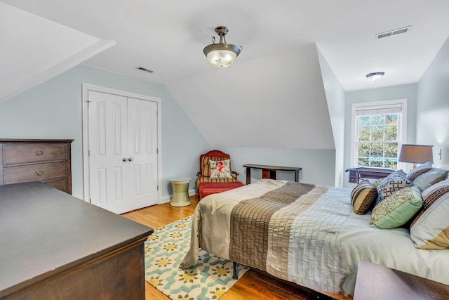 bedroom with visible vents, light wood finished floors, and lofted ceiling