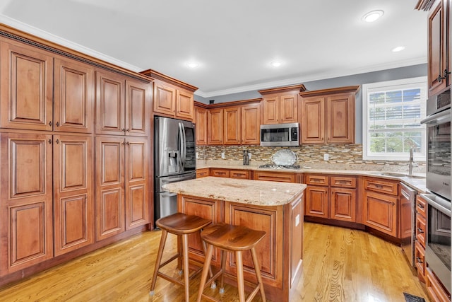 kitchen featuring a center island, a sink, appliances with stainless steel finishes, brown cabinets, and light stone countertops