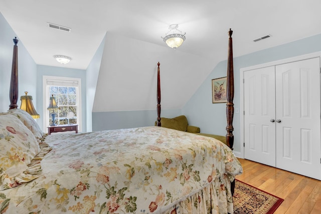 bedroom with visible vents, a closet, vaulted ceiling, and wood finished floors
