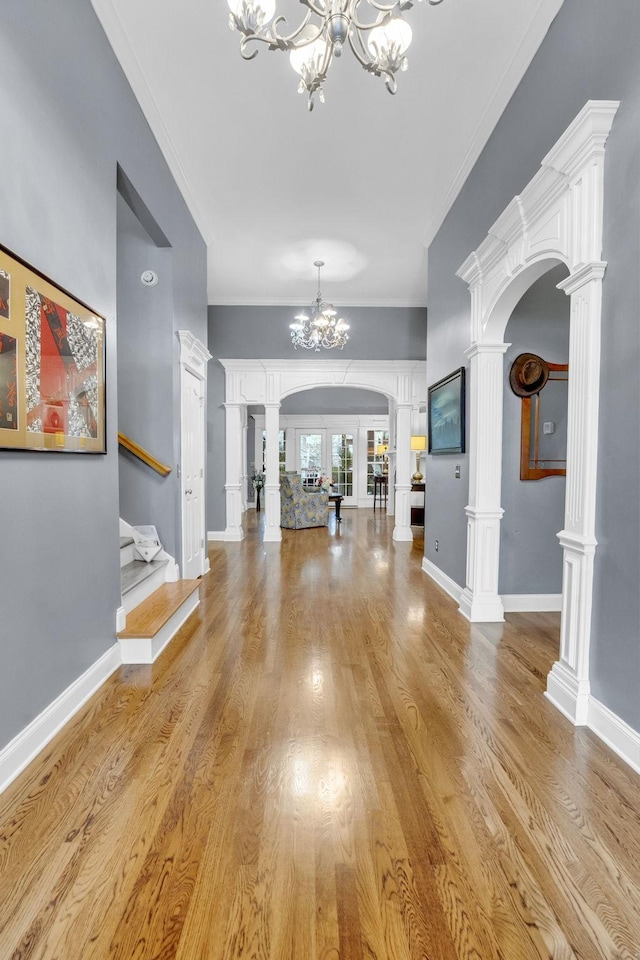 foyer entrance featuring a notable chandelier, baseboards, ornate columns, arched walkways, and light wood finished floors