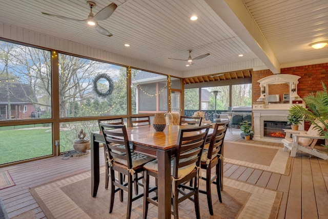 sunroom featuring a glass covered fireplace, a ceiling fan, and outdoor dining space