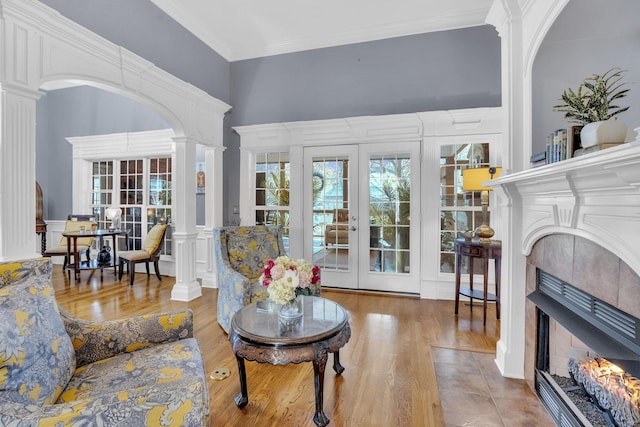 living room with crown molding, a decorative wall, decorative columns, wood finished floors, and a tiled fireplace