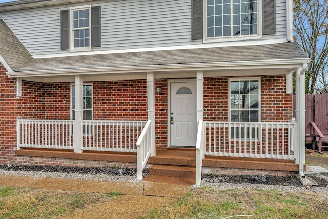 doorway to property featuring roof with shingles, covered porch, and brick siding