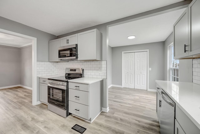 kitchen featuring light wood finished floors, decorative backsplash, light countertops, and stainless steel appliances