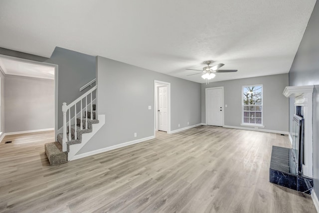 unfurnished living room with baseboards, ceiling fan, light wood-style floors, a fireplace, and stairway
