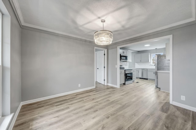 unfurnished living room featuring light wood-style floors, a textured ceiling, ornamental molding, a notable chandelier, and baseboards