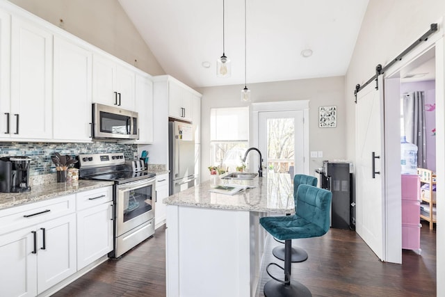 kitchen with a barn door, a sink, vaulted ceiling, stainless steel appliances, and decorative backsplash
