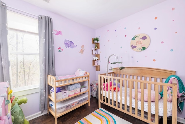 bedroom featuring baseboards, a nursery area, and wood finished floors