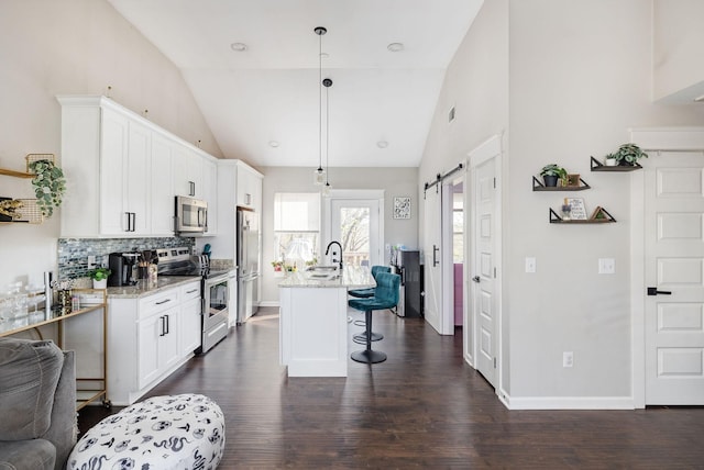 kitchen featuring light stone countertops, a kitchen bar, dark wood-type flooring, a barn door, and appliances with stainless steel finishes