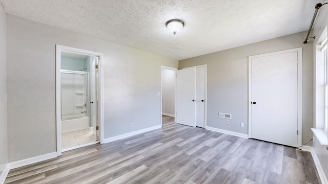 unfurnished bedroom featuring visible vents, ensuite bathroom, baseboards, a textured ceiling, and wood finished floors