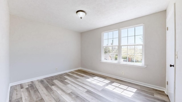 unfurnished room with a textured ceiling, wood finished floors, and baseboards