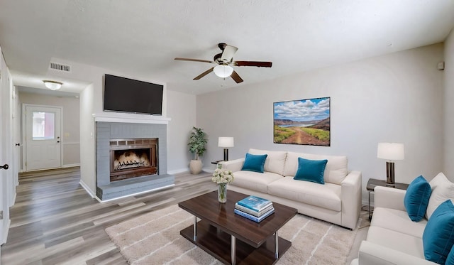 living area featuring wood finished floors, a brick fireplace, a ceiling fan, and visible vents
