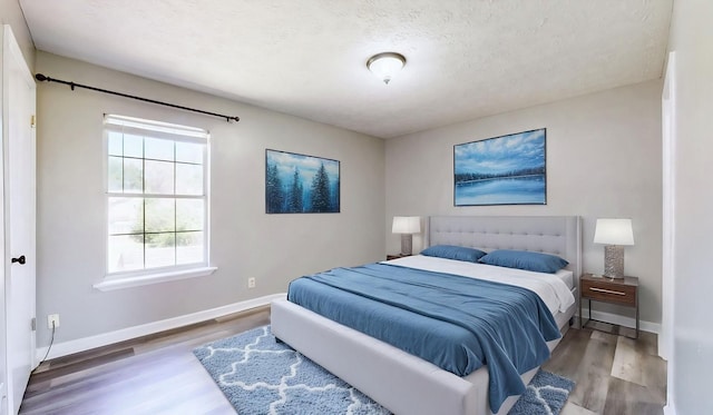 bedroom with a textured ceiling, wood finished floors, and baseboards