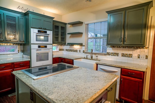 kitchen with a sink, double oven, black electric stovetop, backsplash, and a kitchen island