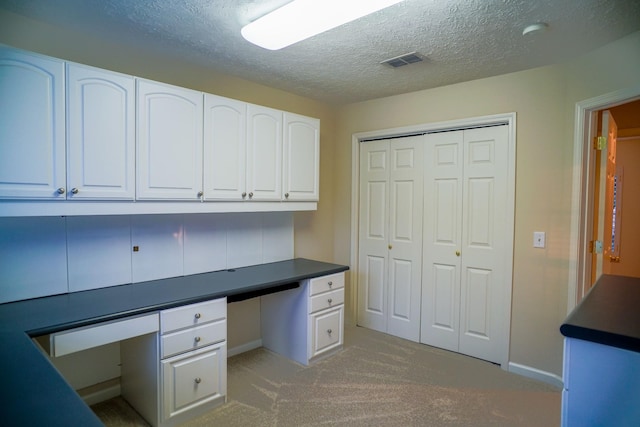 unfurnished office featuring built in study area, light colored carpet, baseboards, and a textured ceiling