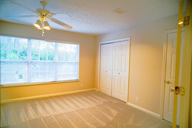 unfurnished bedroom with a textured ceiling, light colored carpet, baseboards, and visible vents